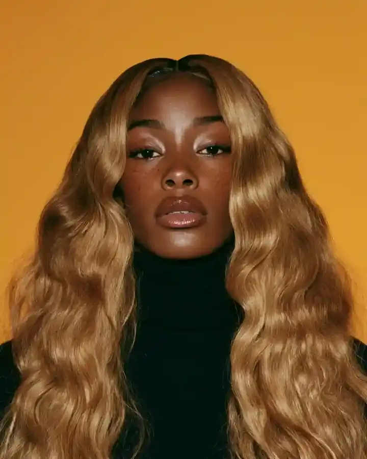 Honey blonde body-wave hair falling in soft S-waves, amber backdrop
