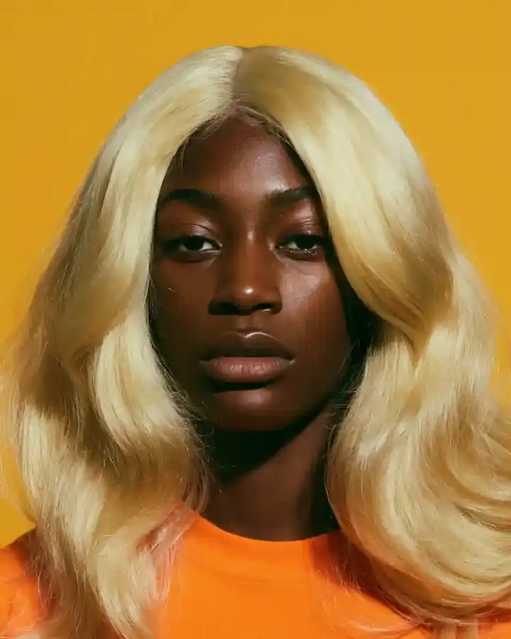 Platinum blonde waves against orange, direct gaze