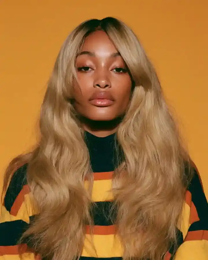 Blonde waves over a striped knit, amber backdrop