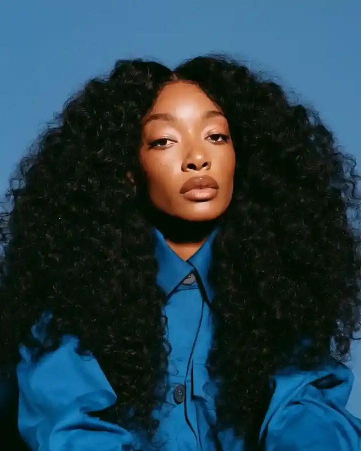 Long defined curls over a blue jacket, blue backdrop