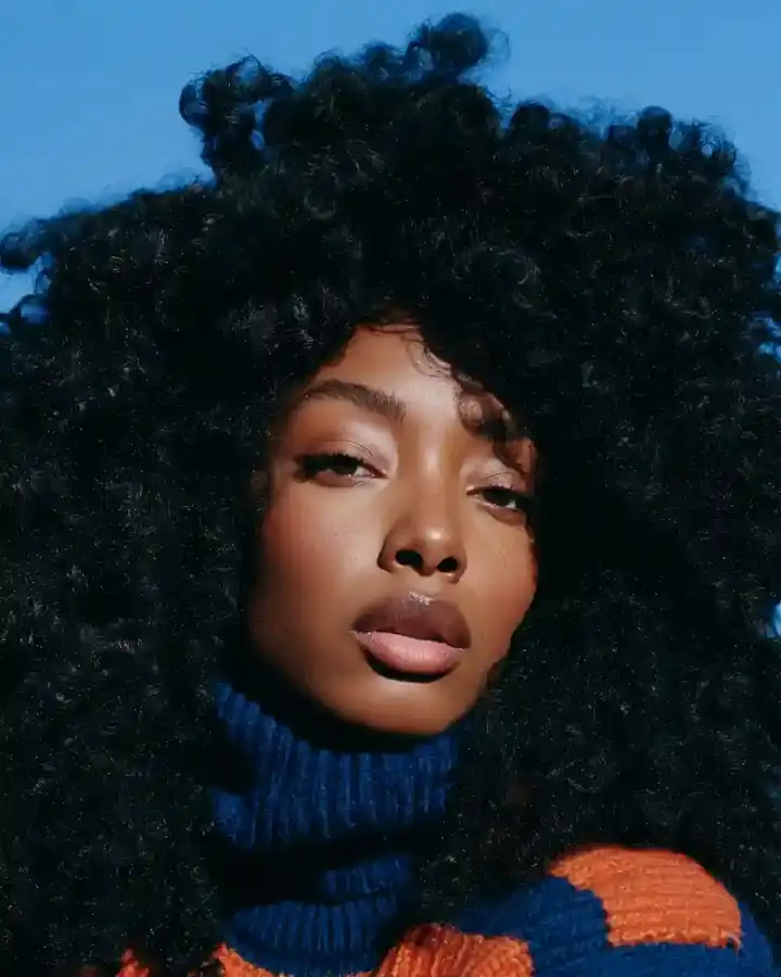 Long dark curls over a colour-blocked knit, blue backdrop