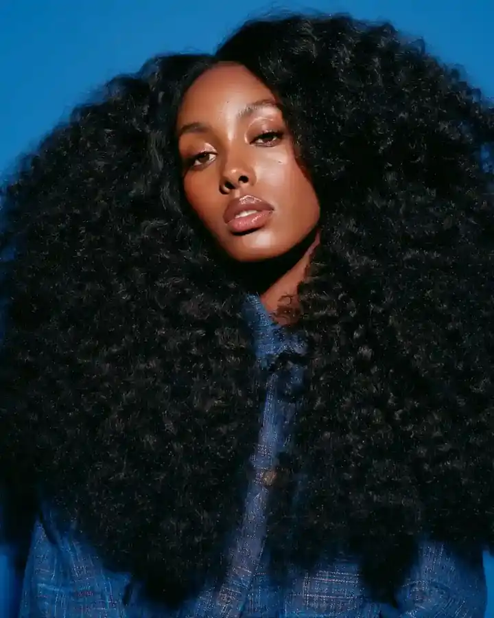 Waist-length dark curls filling the frame, blue backdrop