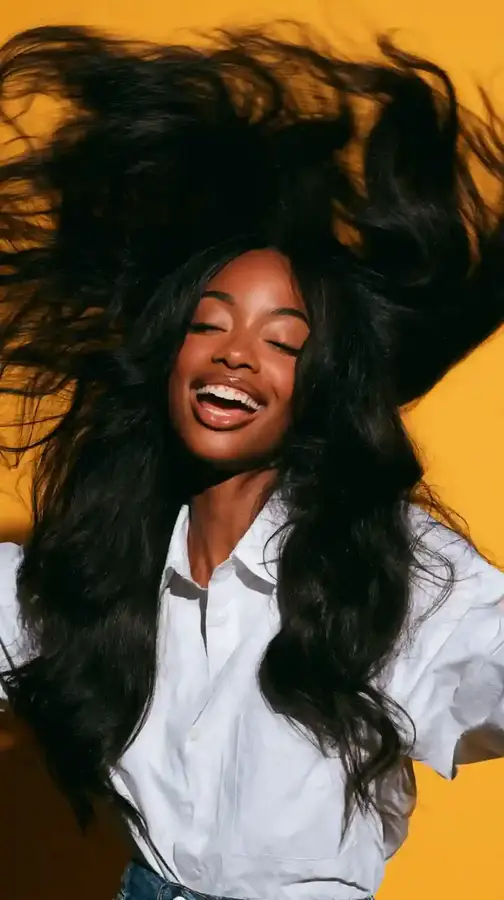 Model mid-laugh flipping long wavy hair, yellow backdrop
