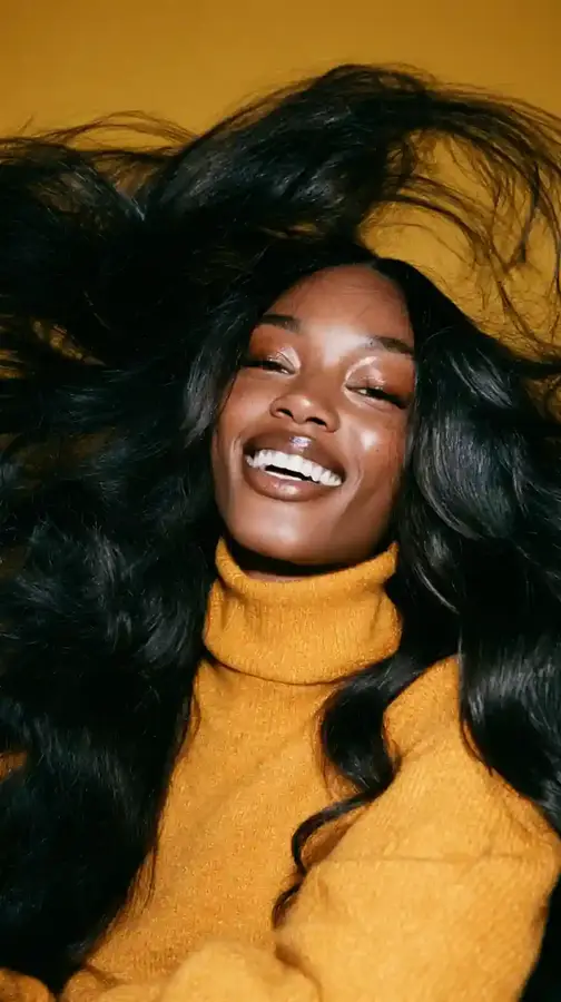 Model mid-laugh flipping long wavy hair, yellow backdrop
