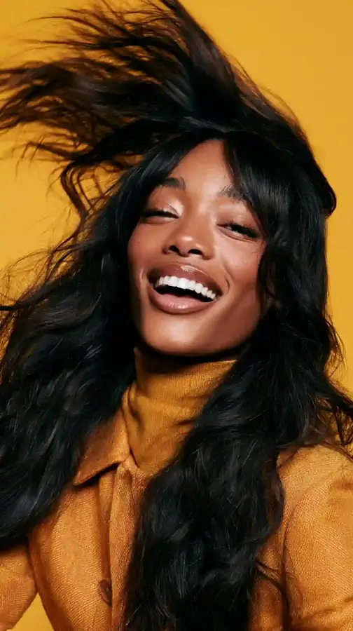 Model mid-laugh flipping long wavy hair, yellow backdrop