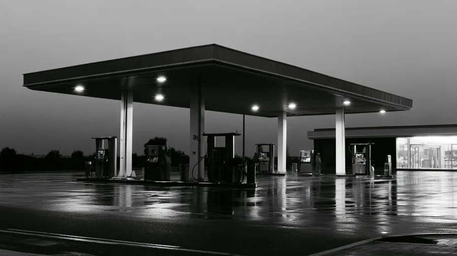 Empty petrol station forecourt at dusk, canopy lights on wet asphalt