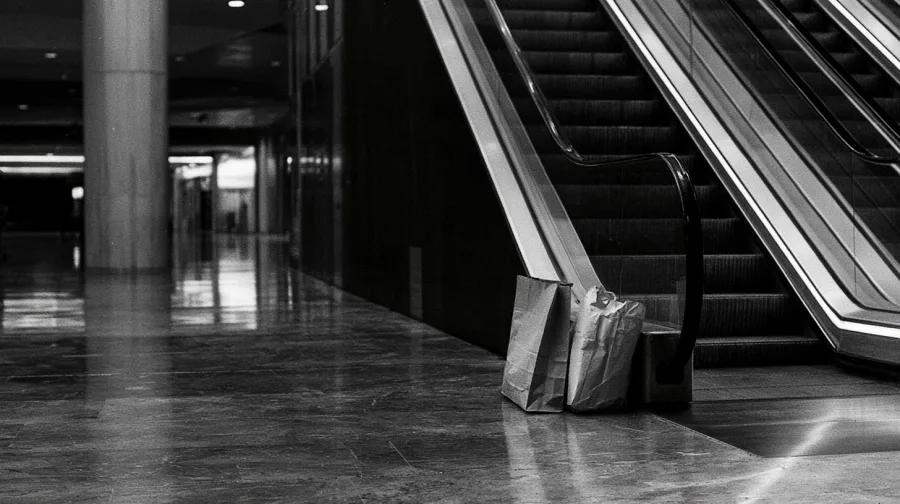 Paper shopping bags left on a marble floor at the foot of a mall escalator