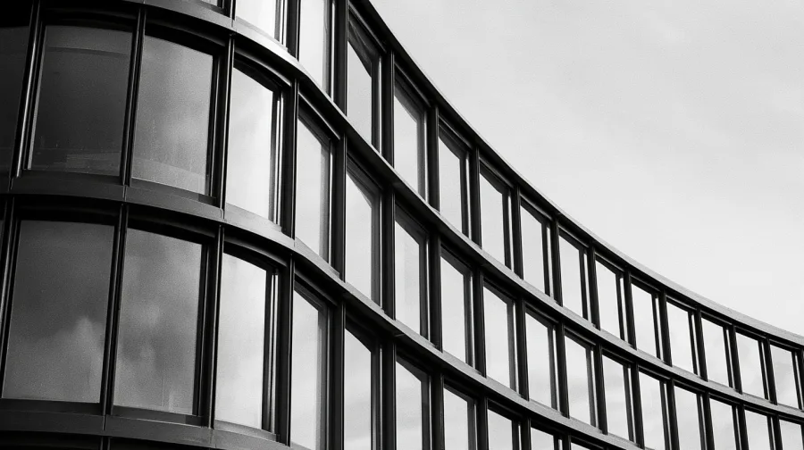 Glass and steel facade of an institutional building, sky reflected in the panels